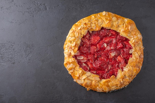 Homemade summer flan pie with strawberries and almond petals on dark background top view with copy