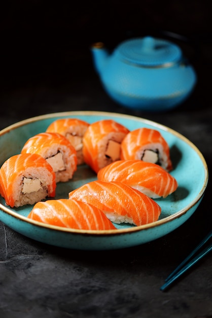 Rotoli di sushi fatti in casa philadelphia e nigiri in un piatto blu su una superficie nera.