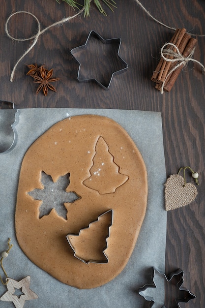 Homemade sweet gingerbread cookies cut from savory spiced pastry dough on wooden table with cutters