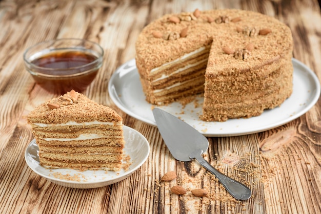 Torta di miele a strati dolce casalinga con le noci sul piatto bianco sulla tavola di legno con la ciotola di miele, di cinammon e di badian.