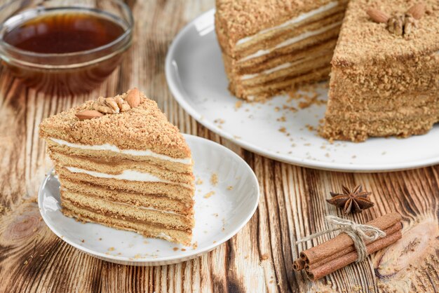 Homemade sweet layered honey cake with nuts on white plate on wooden table with bowl of honey, cinammon and badian.