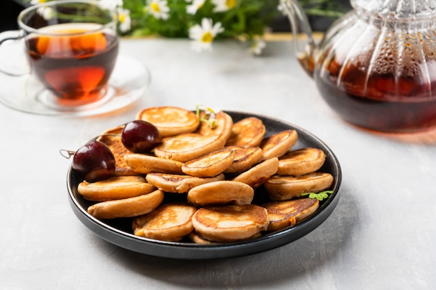 Homemade sweet mini pancakes with cherry jam and aromatic tea.