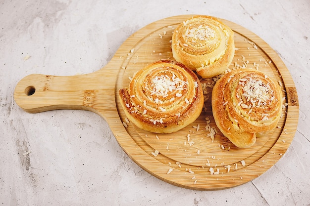 Homemade sweet three buns with coconut, photographed from above on a wooden board, concrete gray background (Selective focus). Coconut rolls in the form of rolls. Without people.