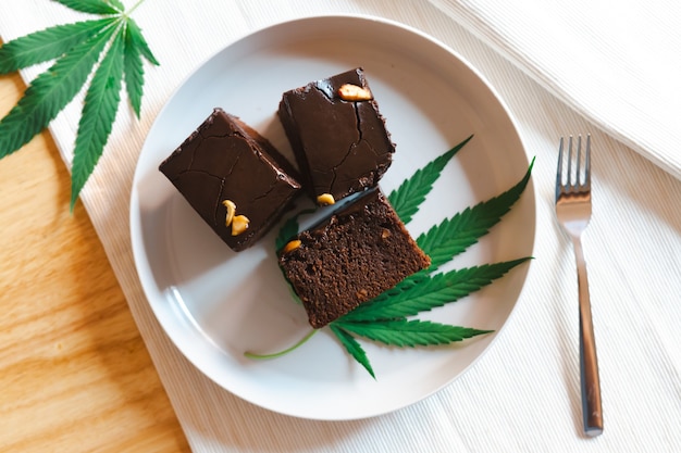 Homemade sweetmeat with marijuana or cannabis leaf on white plate. Alternative medicine concept.