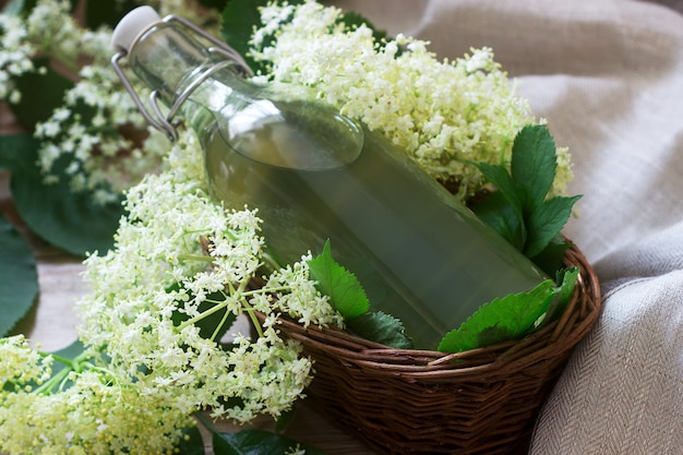 Homemade syrup of elderberry flowers in a glass jar and elder branches on a wooden table Rustic style.