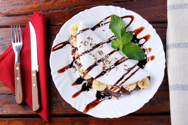 Homemade tapioca or beiju stuffed with banana and chocolate on white plate over rustic wooden table