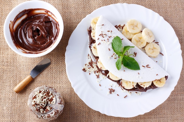 Homemade tapioca or beiju stuffed with banana and chocolate on white plate over rustic wooden table