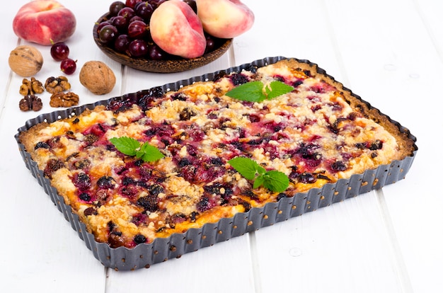 Домашний пирог с ягодами, фруктами и грецкими орехами в форме на светлом фоне.