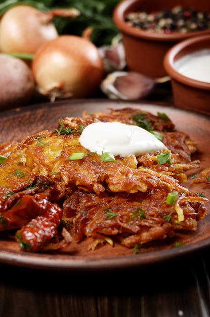 Homemade tasty potato pancakes in clay dish with sundried tomatoes and sour cream