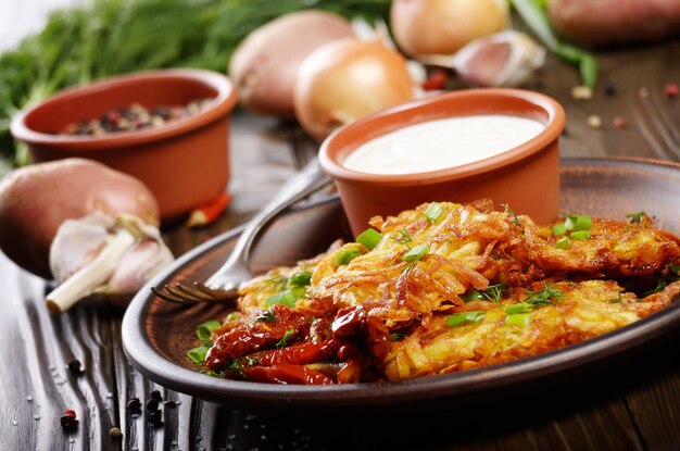 Homemade tasty potato pancakes in clay dish with sundried tomatoes and sour cream