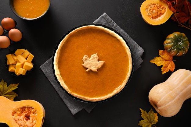 Homemade tasty pumpkin pie with autumn decorations and leaves for Thanksgiving Day on black