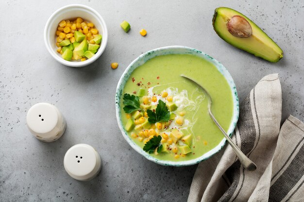 Homemade tender soup puree from avocado and corn with cream in rustic ceramic plate on gray concrete old surface