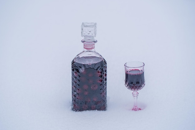 ガラス瓶と雪と白の背景にワインクリスタルガラスの赤い桜の自家製チンキ