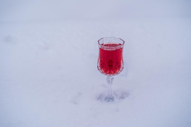 雪と白の背景にワインクリスタルガラスの赤い桜の自家製チンキ