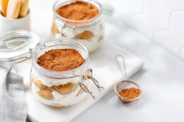 Homemade tiramisu dessert in jars Italian dessert with cream and cocoa Marble board Copy space