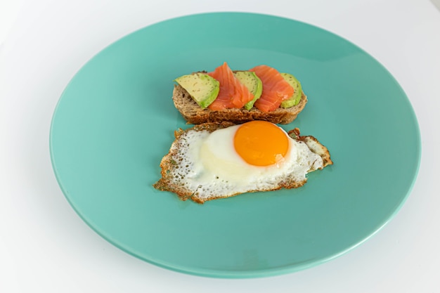 Домашний тостовый бутерброд с лососем и авокадо на ломтике зернового хлеба. Жареные яйца с ярким желтком на мятном фоне.