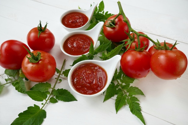 Homemade tomato sauce in a white sauce-pan set and fresh ripe tomatoes with leaves