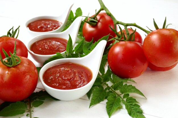 Homemade tomato sauce in a white sauce-pan set and fresh ripe tomatoes with leaves