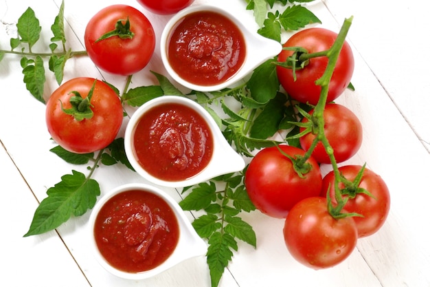 Homemade tomato sauce in a white sauce-pan set and fresh ripe tomatoes with leaves