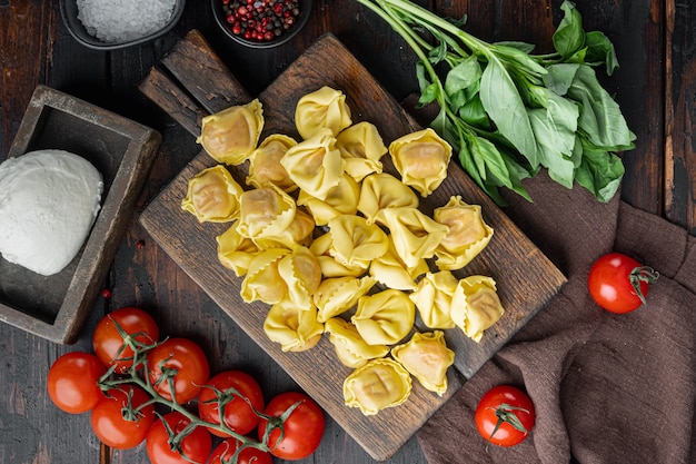 Photo homemade tortellini with cheese and basil set, on wooden cutting board, on old dark wooden table, top view flat lay