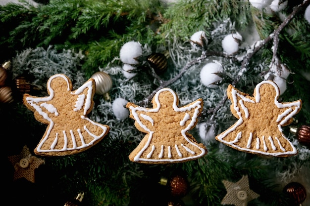 Homemade traditional Christmas gingerbread cookies with icing ornate. Three gingerbread angels with xmas decorations and fir tree