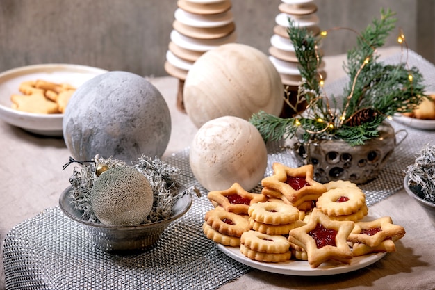 Homemade traditional Christmas Linz shortbread biscuits cookies with red jam on plate. Trend Wooden eco-friendly xmas decorations on linen tablecloth. Holiday table setting.