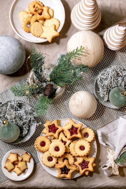 Homemade traditional Christmas Linz shortbread biscuits cookies with red jam on plate. Trend Wooden eco-friendly xmas decorations on linen tablecloth. Holiday table setting.