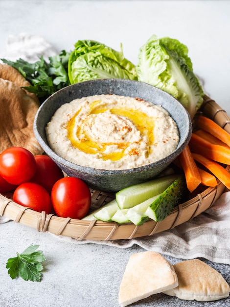 Homemade traditional spread hummus dip served with fresh vegetable , pita and herbs in tray.