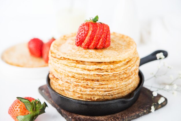 Homemade traditional thin pancakes with berries on a white surface
