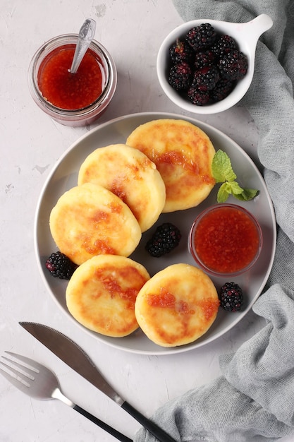 Homemade traditional Ukrainian dish syrniki with berry jam and blackberry on grey plate on light background