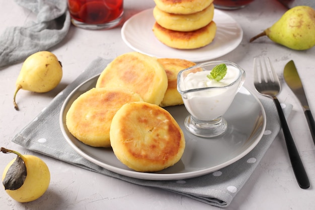 Homemade traditional Ukrainian dish syrniki with sour cream on grey plate on light background