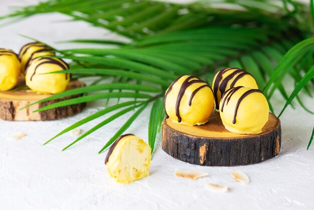 Homemade truffles with pineapple and mango with a palm branch on a light background