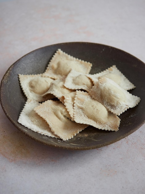 Homemade uncooked freshly prepared Italian ravioli pasta in a dark plate