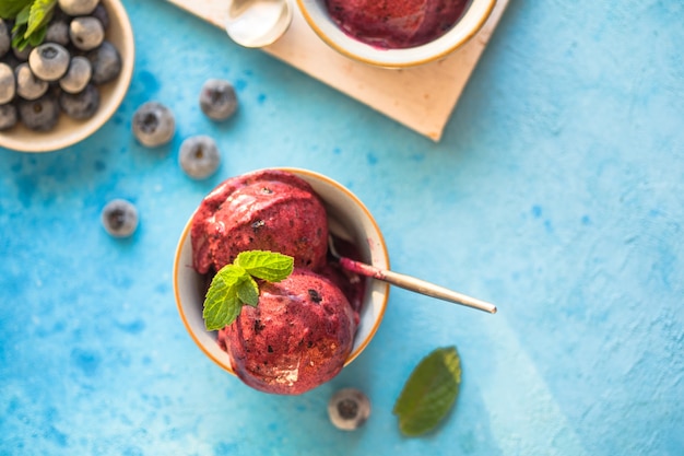 Foto gelato vegano fatto in casa alla banana o gelato con mirtillo in una ciotola su sfondo blu. dolce sano.