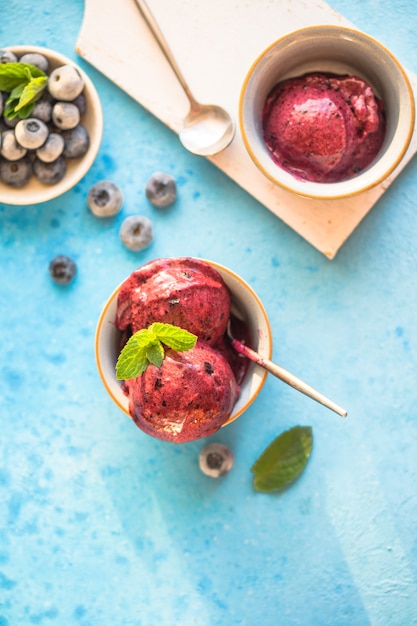 Photo homemade vegan banana ice cream or gelato with blueberry in a bowl  on blue  background. healthy dessert.