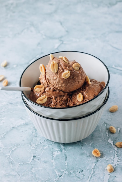 Homemade vegan peanut butter banana and chocolate ice cream in a bowl with peanuts over gray marble background
