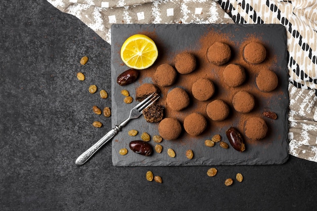 Homemade vegan truffles with dried fruits, walnuts and raw cocoa powder served on black slate plate.