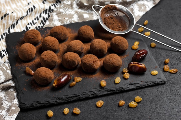 Photo homemade vegan truffles with dried fruits, walnuts and raw cocoa powder served on black slate plate.