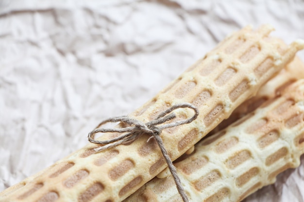 Homemade wafer rolls tied with jute on crumpled baking paper.