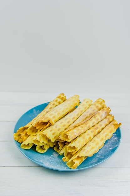 Tubi di waffle fatti in casa su un piatto blu su sfondo bianco con spazio per le copie