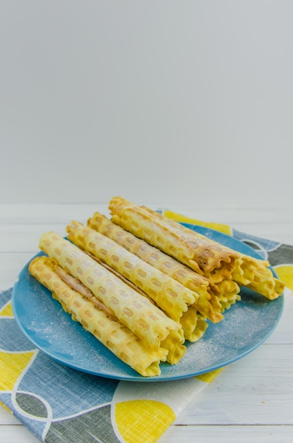 Tubi di waffle fatti in casa su un piatto blu su sfondo bianco con spazio per le copie