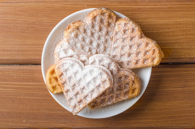 Homemade waffles heart sprinkled with powdered sugar on plate on a wooden table.