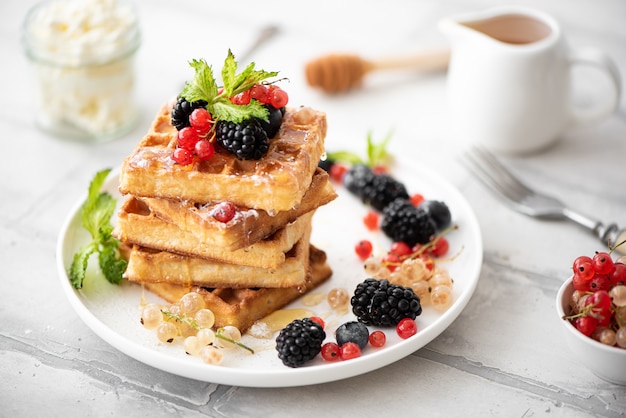 Homemade waffles with berries and honey on a white plate