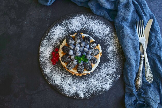 homemade waffles with blueberries and blackberries, powdered sugar on a stone plate with fruit. Shallow depth of field.