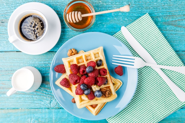 Homemade waffles with raspberries and blueberry, cup of coffee, milk and cutlery