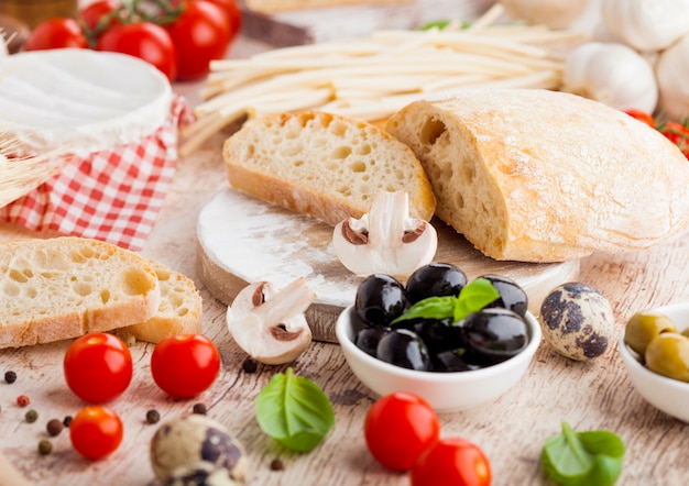 Homemade wheat bread with quail eggs and raw wheat and fresh tomatoes. Classic italian village food. Garlic, black and green olives. Wooden spatula