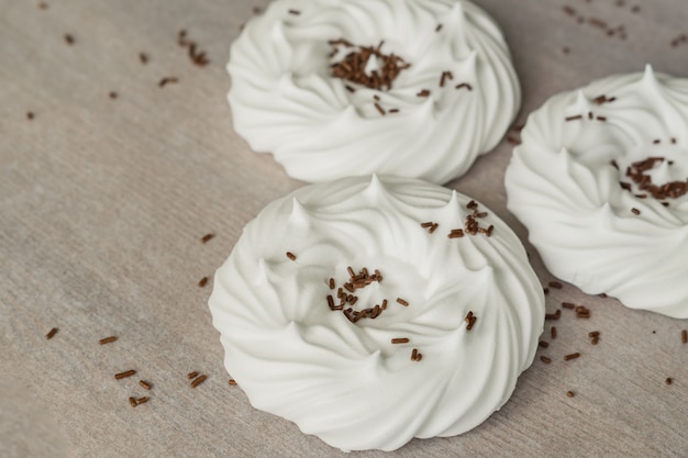 Homemade white air meringues and chocolate confectionery decorations on parchment paper.