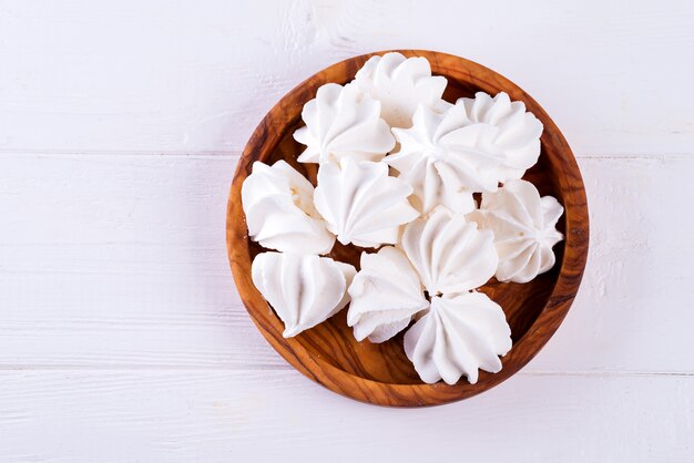 Homemade white meringue in wooden plate on white wood