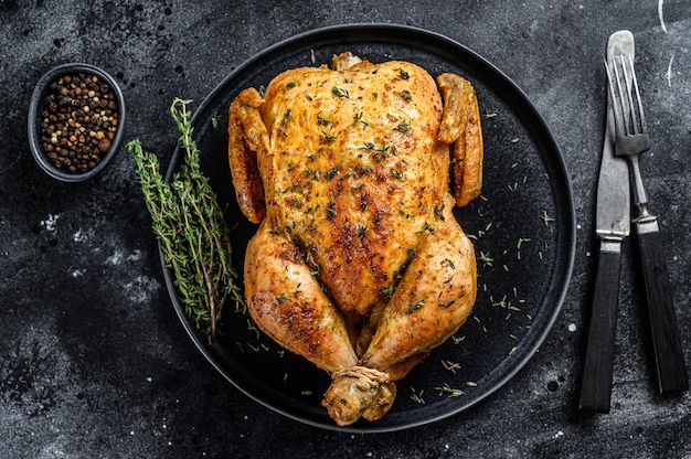 Homemade whole baked chicken rotisserie with thyme.  Black background. Top view.