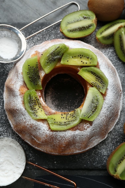 Homemade yogurt cake with kiwi and powdered sugar on black table flat lay